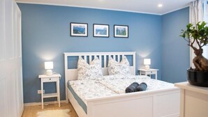A bedroom with a white bed, two bedside tables with lamps, a white furry rug, and a potted plant. - Fewo Am Sommerberg by Interhome (Donaueschingen)
