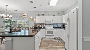 Una cucina moderna con mobili bianchi, un'isola con piano di lavoro nero e un'isola centrale con posti a sedere. Sono presenti lampade a sospensione, un forno a microonde e un frigorifero.