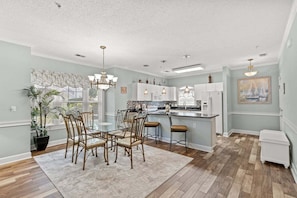 A spacious kitchen with a central island, white cabinetry, and a dining area with wooden chairs and a glass table. - Magnolia North 4847-105 (Myrtle Beach)