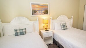 A hotel room with two beds, a nightstand with a lamp, and a painting of a beach scene. - World Tour 104-202a (Myrtle Beach)