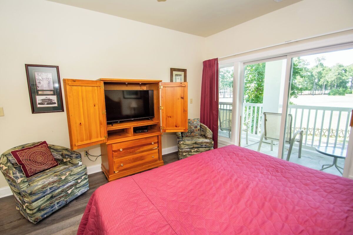 Ein Schlafzimmer mit einem großen Bett, einer Holz-Unterhaltungseinrichtung mit Fernseher und einem Balkon mit Blick auf Grünflächen.