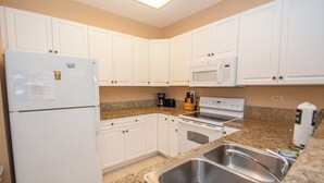 A compact kitchen with white cabinets, a built-in microwave, a stove, and a refrigerator. - World Tour 104-202a (Myrtle Beach)