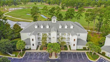 A multi-story hotel with a central courtyard, surrounded by lush greenery and a golf course.
