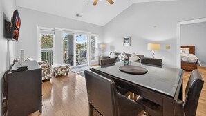 A spacious living area with a large dining table, comfortable seating, a ceiling fan, and a view through the glass doors to the outdoors. - World Tour 1009-302 (Myrtle Beach)