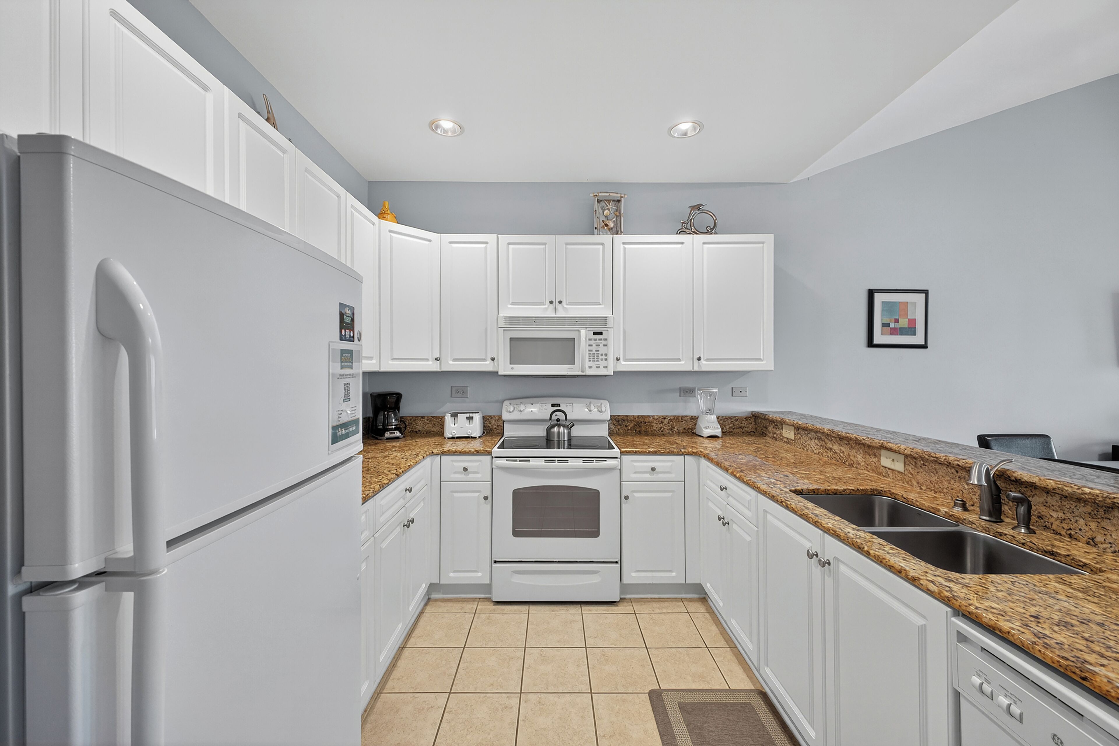 A modern kitchen with white cabinets, a granite countertop, a built-in microwave, and a stainless steel sink.