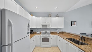 A modern kitchen with white cabinets, a granite countertop, a built-in microwave, and a stainless steel sink. - World Tour 1009-302 (Myrtle Beach)