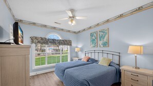 Une chambre avec deux lits, un ventilateur de plafond, une fenêtre donnant sur une pelouse verdoyante et des œuvres d’art accrochées aux murs.