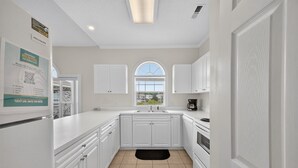 A modern kitchen with white cabinetry, a large window, and a black rug. - Magnolia Place 4687-304 (Myrtle Beach)