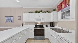 A modern kitchen with white cabinetry, a stainless steel stove, a microwave, and a sink. - Magnolia Place 4765-303 (Myrtle Beach)