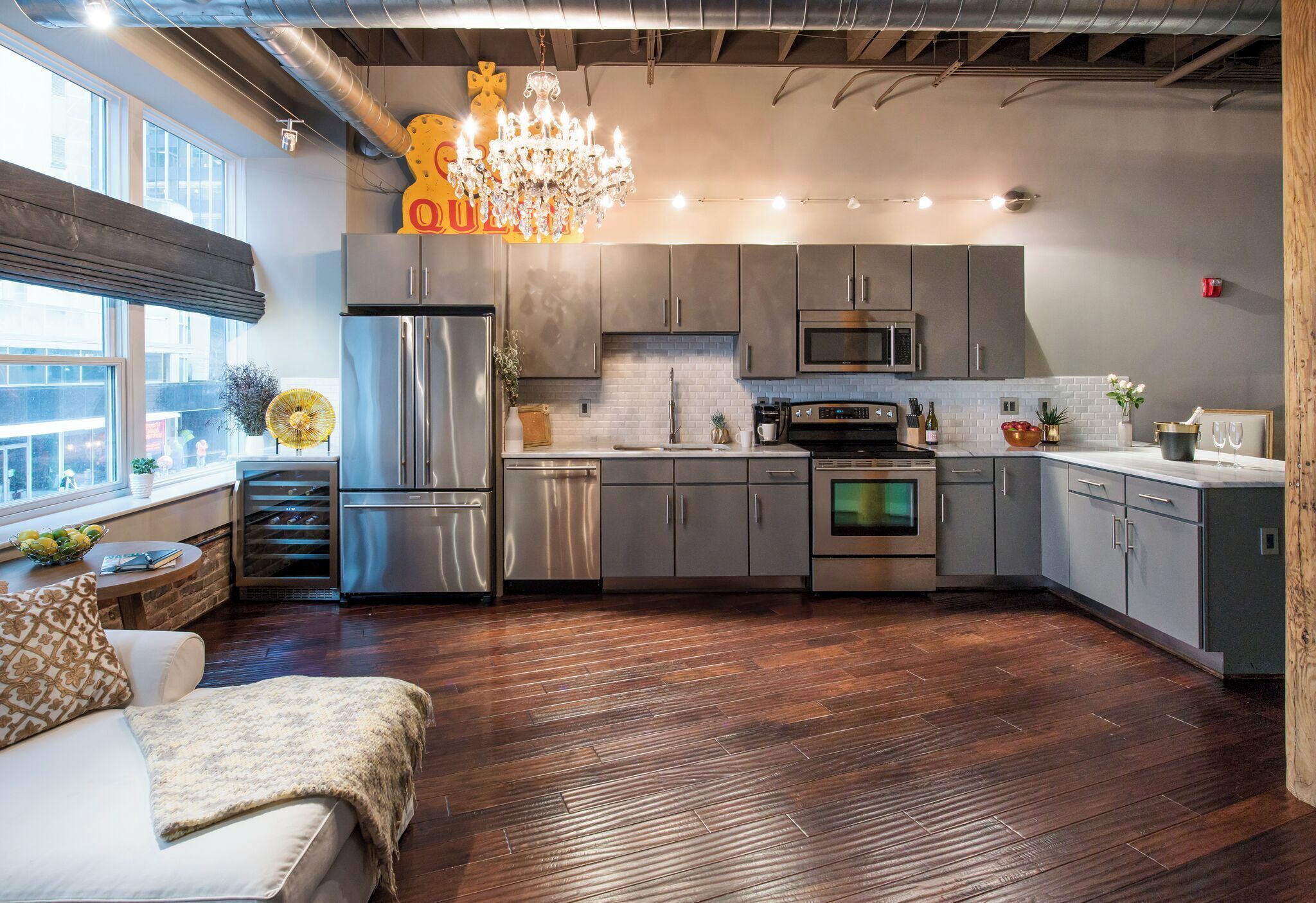 A modern kitchen with stainless steel appliances, grey cabinets, and a chandelier.