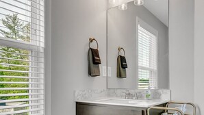 A bathroom with a large mirror, a sink, and a vanity cabinet. There is a window with blinds, and a towel rack with towels. - Tee Time Treasures in Sango 1625 Gold Club Ln, #602 (Nashville)