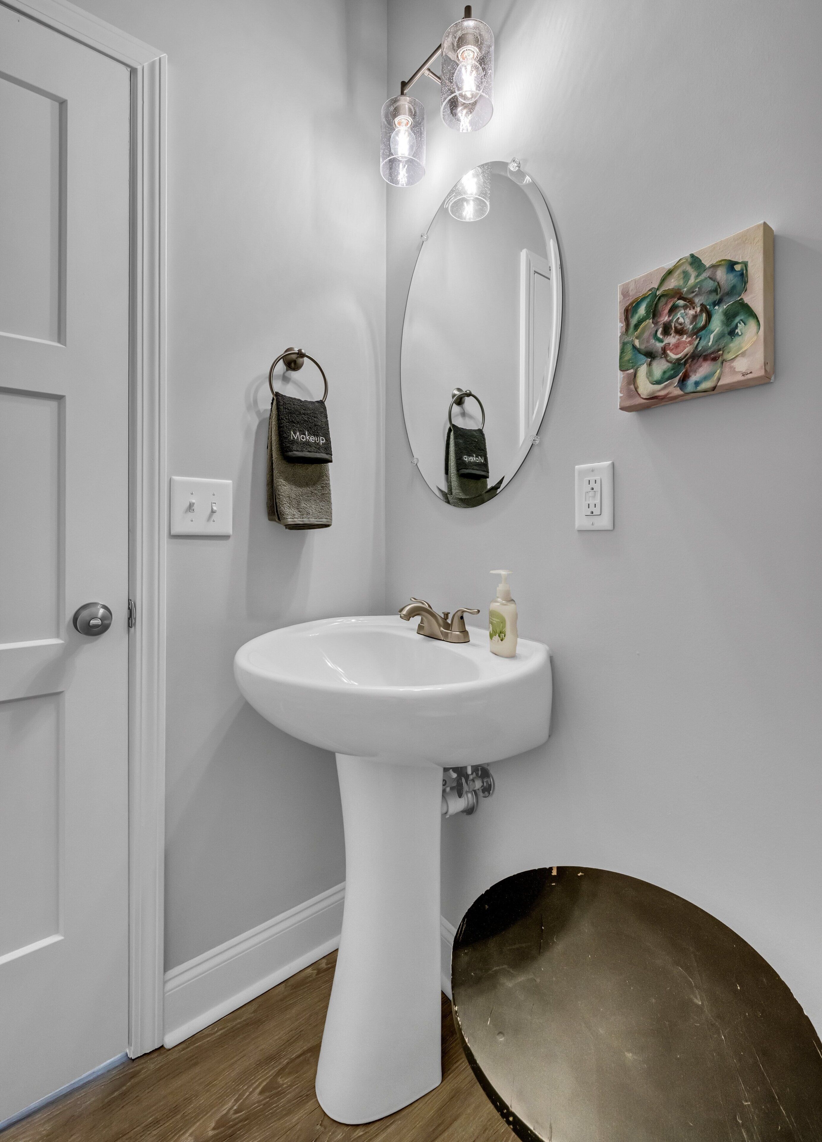 A bathroom with a white pedestal sink, a mirror, and a wall-mounted light fixture.