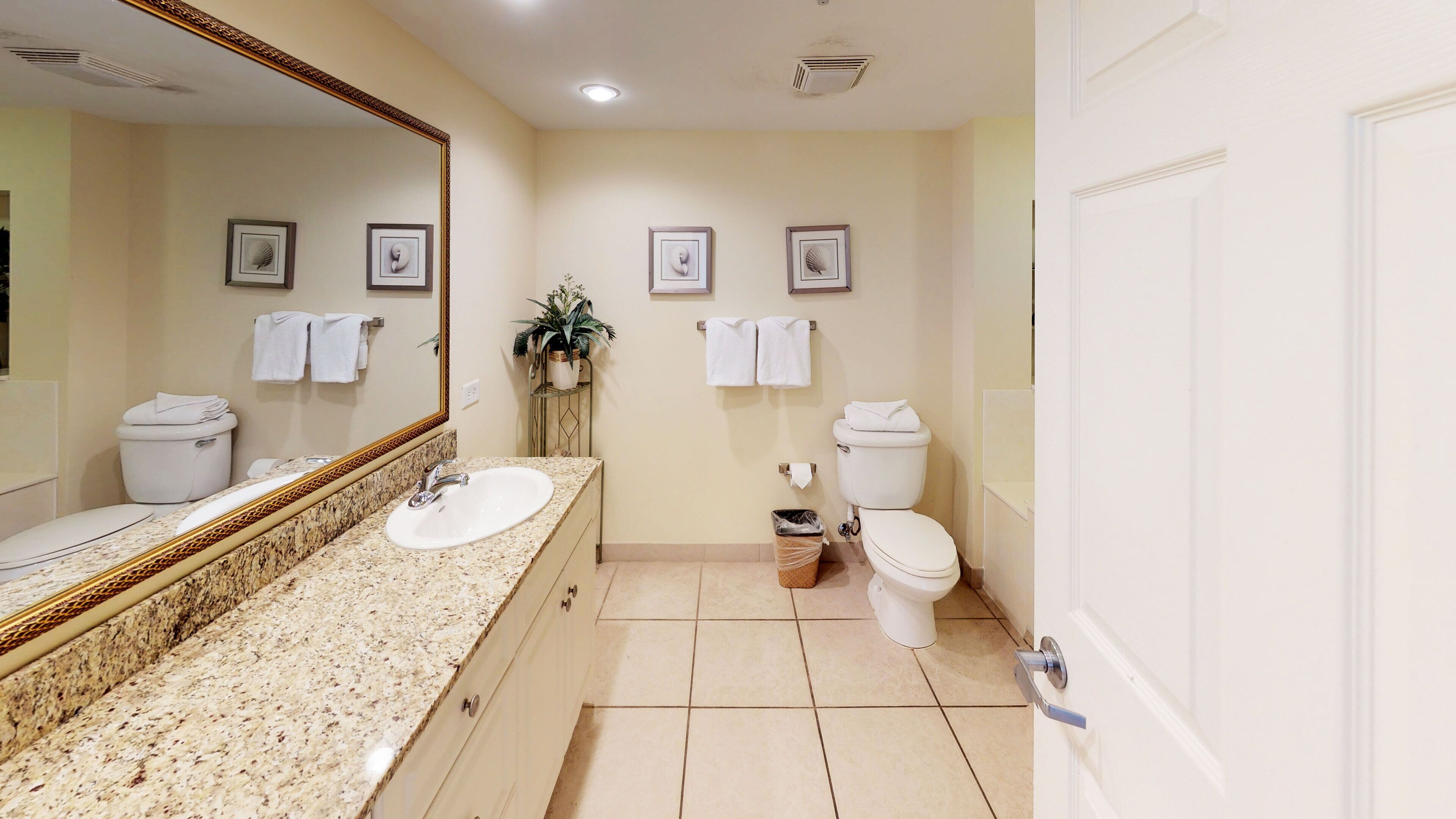 A bathroom with a granite countertop sink, two toilets, and a large mirror.
