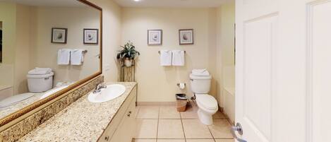 A bathroom with a granite countertop sink, two toilets, and a large mirror.