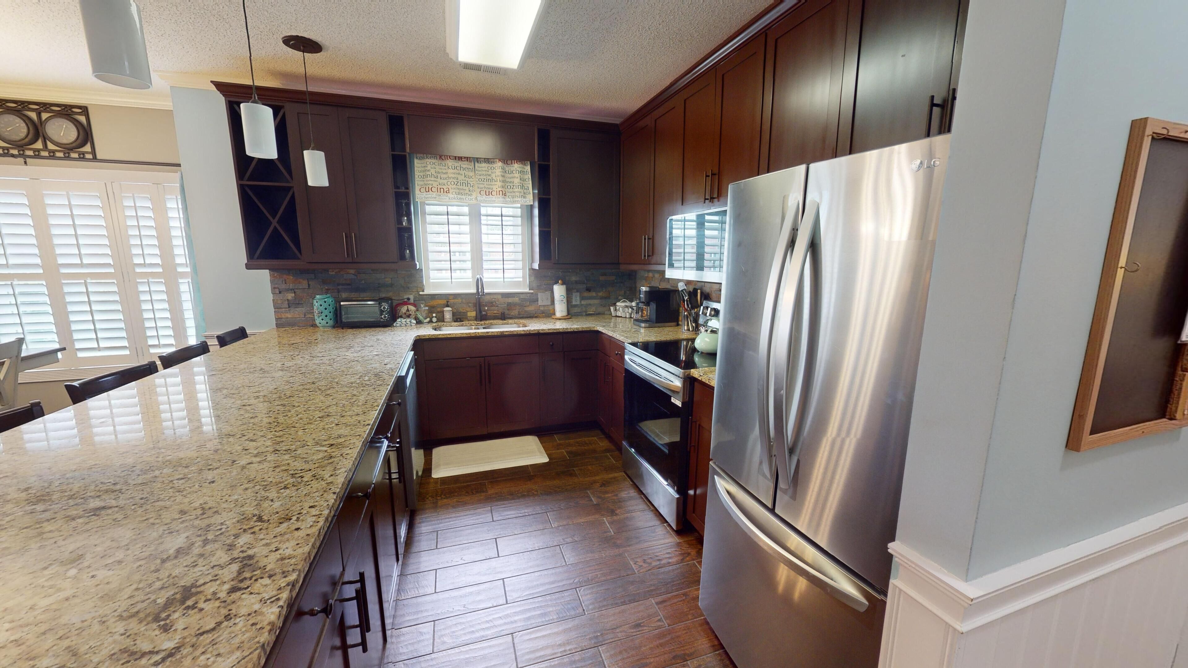 A modern kitchen with dark wooden cabinets, a stainless steel refrigerator, and a granite countertop.