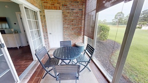 A covered patio with a brick wall, a white door, and a view of a grassy area. - Magnolia North Unit 105 (Myrtle Beach)