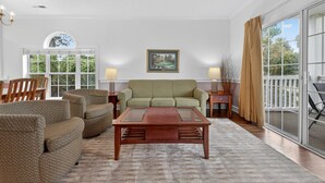 Un salon avec un canapé vert, deux fauteuils, une table basse en bois et un tableau accroché au mur.