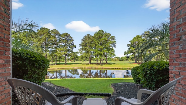 A view from a porch with two chairs facing a pond, surrounded by trees and a grassy area. - Magnolia North 4843-103 (Myrtle Beach)