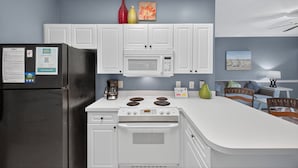 A modern kitchen with white cabinets, a black refrigerator, a microwave, a stove, and a dining area with a table and chairs. - Magnolia North 4843-103 (Myrtle Beach)