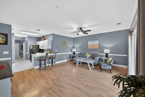 A modern living room with a grey sofa, a coffee table, and a dining area with a kitchen in the background. - Magnolia North 4843-103 (Myrtle Beach)