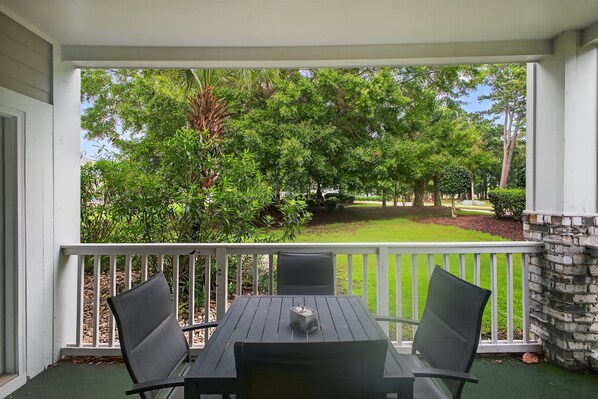 A covered patio with a table and chairs, overlooking a well-maintained lawn and trees. - Magnolia Place 4757-104 (Myrtle Beach)