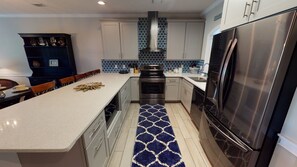 A modern kitchen with a central island, stainless steel appliances, and a patterned backsplash. - Magnolia North Unit 104 (Myrtle Beach)