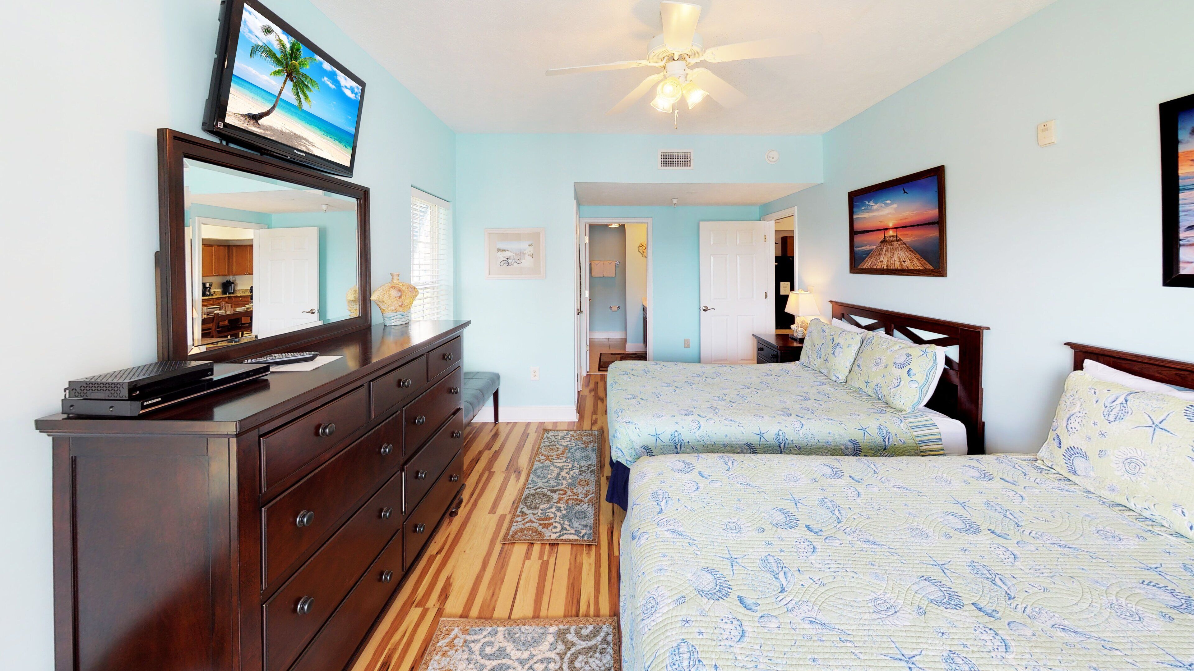 Un dormitorio con cama, cómoda, televisor y ventilador de techo.