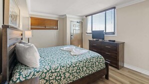 A bedroom with a bed, a dresser, a television on the dresser, a door, and a window with blinds. - Meridian Plaza 1401 (Myrtle Beach)
