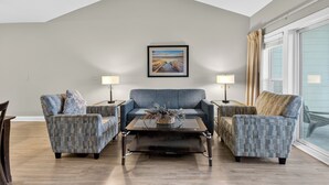A living room with a high ceiling, a large window with curtains, a sofa, two armchairs, a coffee table, and two lamps. - World Tour 104-303 (Myrtle Beach)