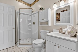 Un baño con ducha de vidrio, inodoro blanco, lavabo con tocador y espejo sobre el lavabo.