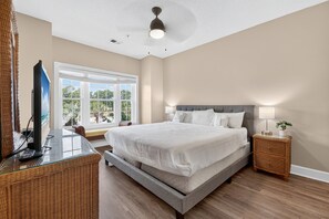 Un dormitorio con una cama grande, un televisor sobre una mesita de vidrio y una mesita de noche con una lámpara.