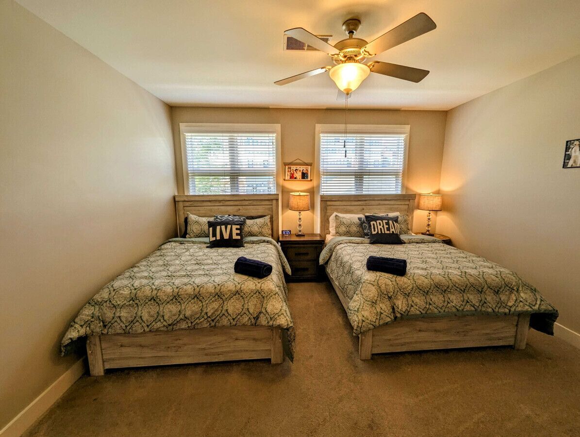 A bedroom with two beds, a ceiling fan, and two bedside lamps.