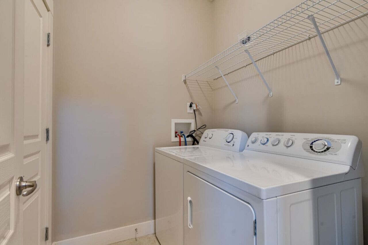 A laundry room with a front-loading washer and dryer, a metal drying rack, and a power outlet on the wall.
