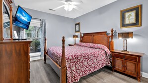 A bedroom with a bed, wooden nightstands, a ceiling fan, a TV, and a window with curtains. - World Tour 116-104 (Myrtle Beach)