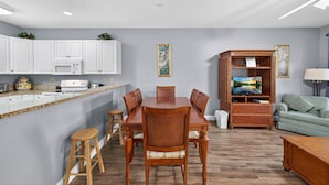 A modern kitchen with white cabinets, a granite countertop, and a dining area with wooden chairs. - World Tour 116-104 (Myrtle Beach)