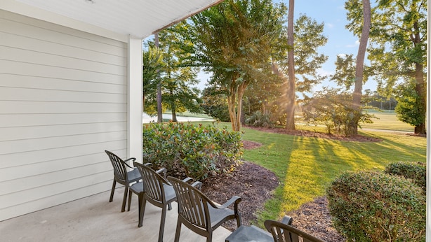 A covered patio with outdoor seating and a view of a well-maintained lawn and trees. - World Tour 116-104 (Myrtle Beach)