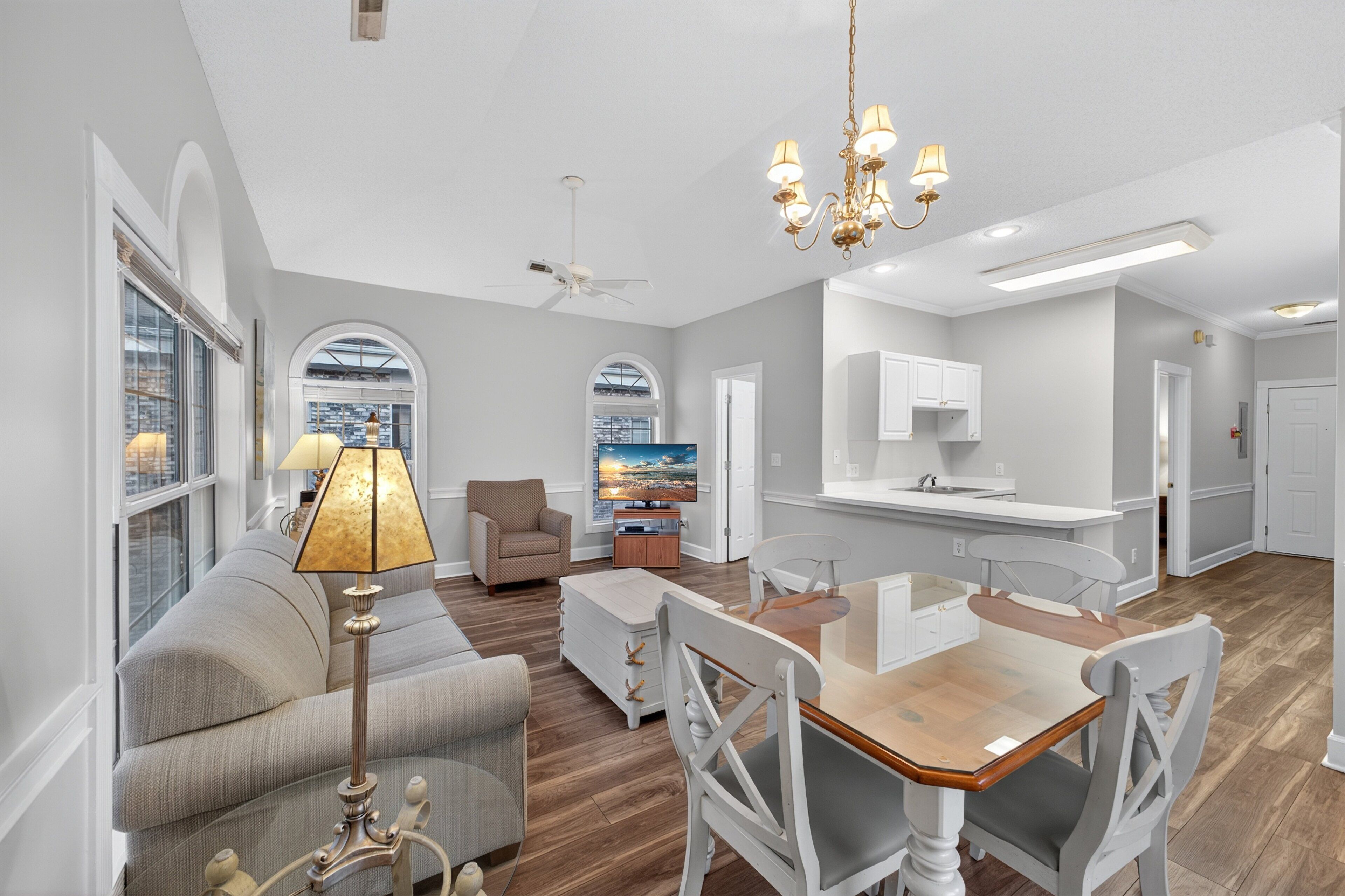 A spacious living room with a sofa, a dining table, and chairs, a kitchen area, and a large window with a view.