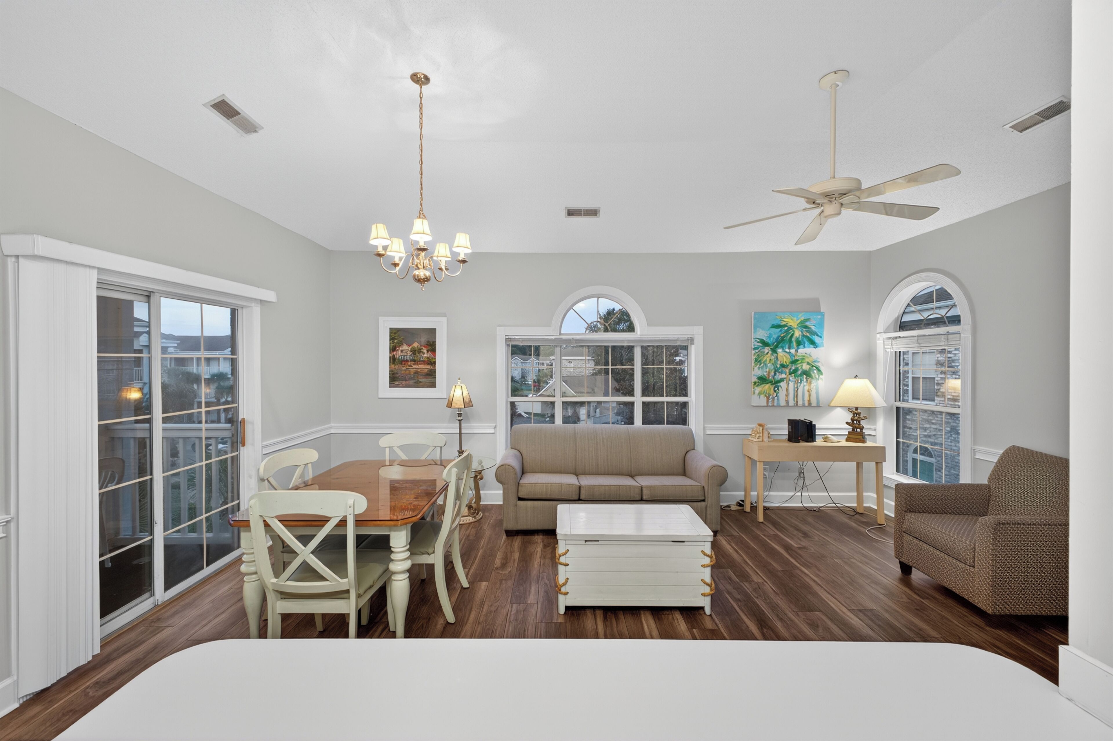 A spacious living room with a large sofa, a dining table with chairs, a coffee table, and a ceiling fan.