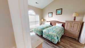A bedroom with two beds, a wooden cabinet, a nightstand, a lamp, and a window with blinds. - Magnolia Place 4687-302 (Myrtle Beach)