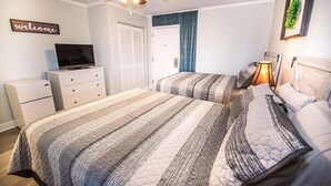 Ein Schlafzimmer mit einem Bett, einem Fernseher auf einer Kommode, einem Deckenventilator und einem Schild mit der Aufschrift 'welcome' an der Wand.