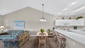 Een moderne keuken met witte kasten, een centraal eiland en een zithoek met een bloemenbank en houten stoelen.