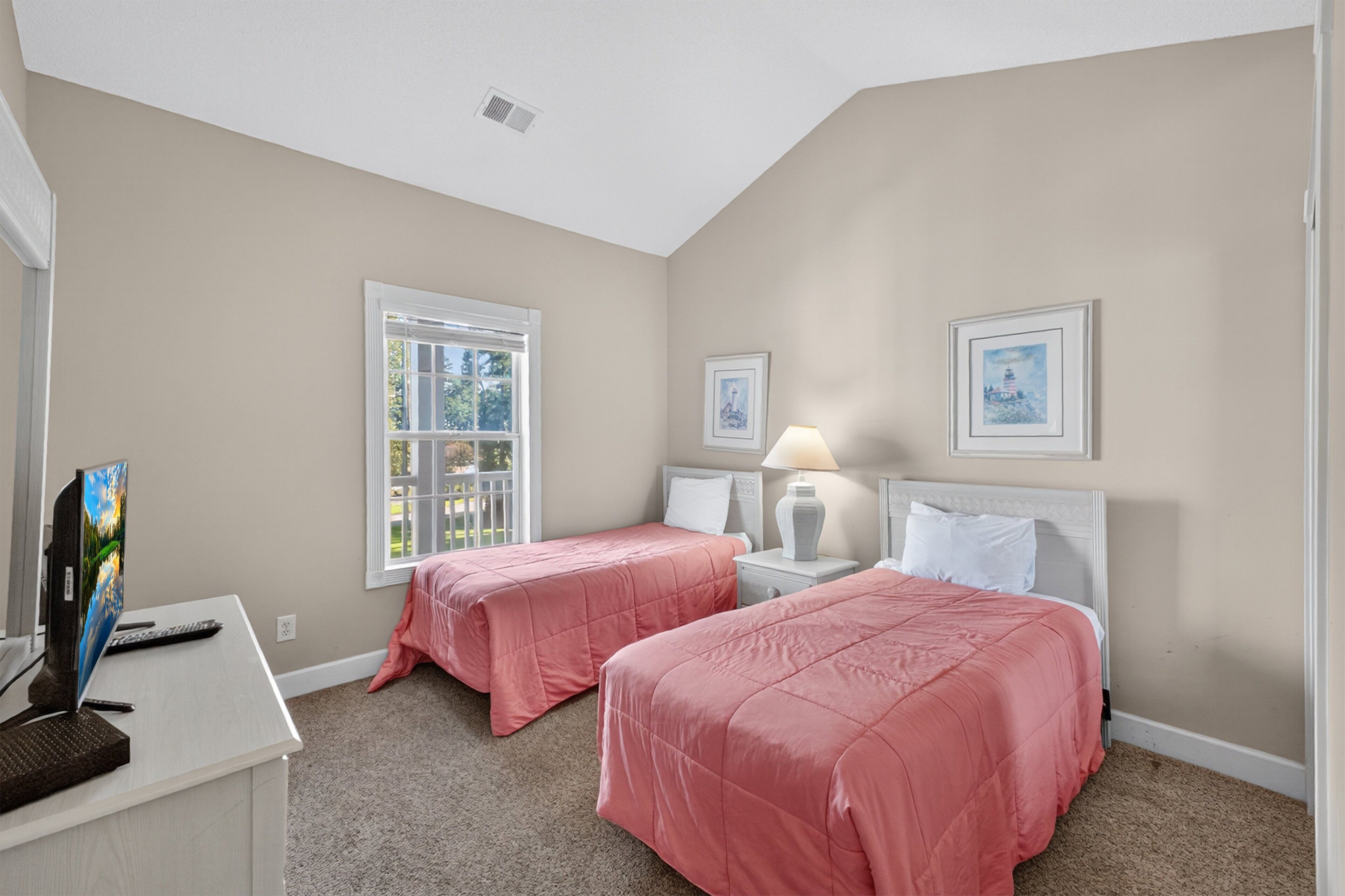 A bedroom with two beds, a desk with a computer, and a window.