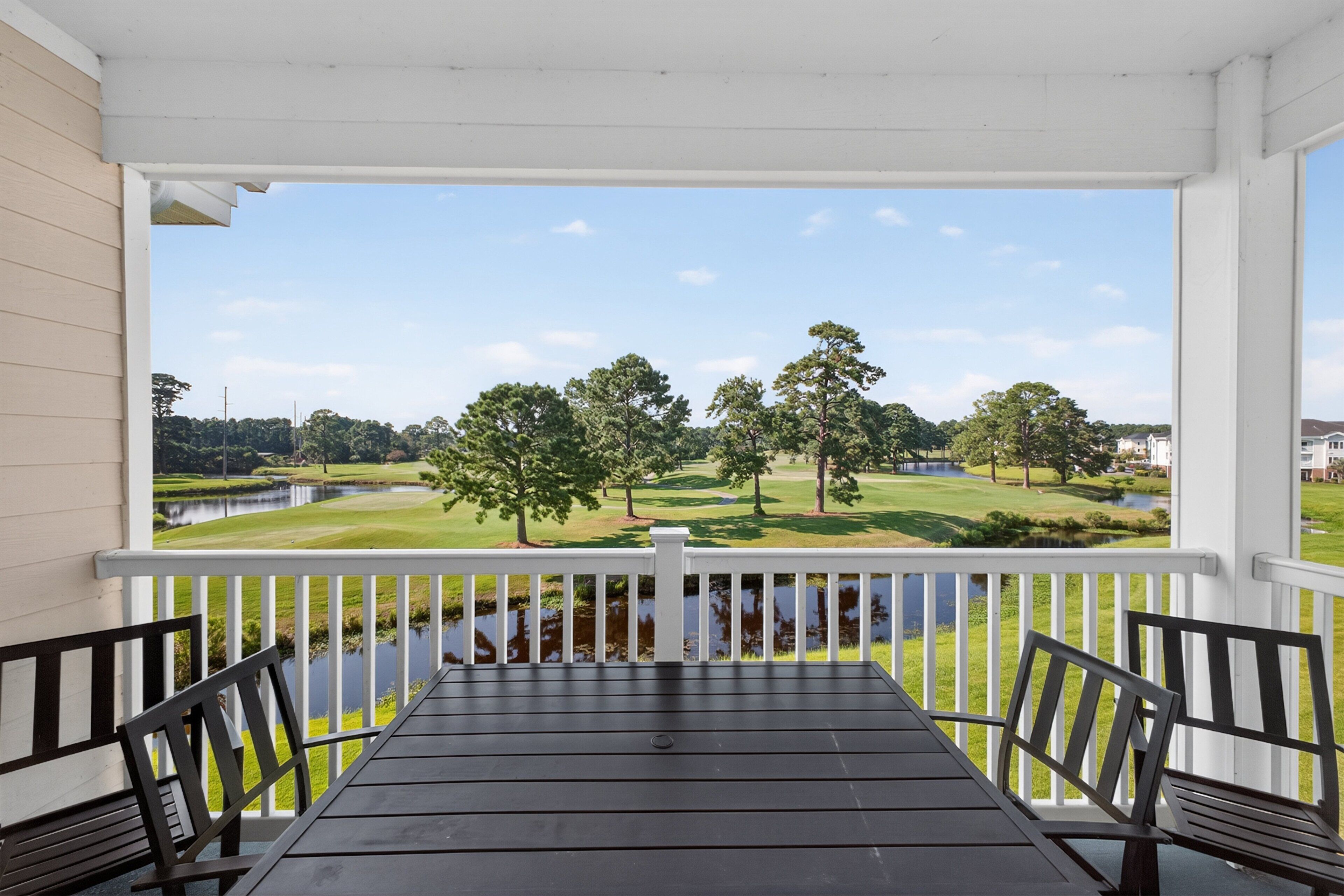 A covered porch with a view of a golf course and a body of water.