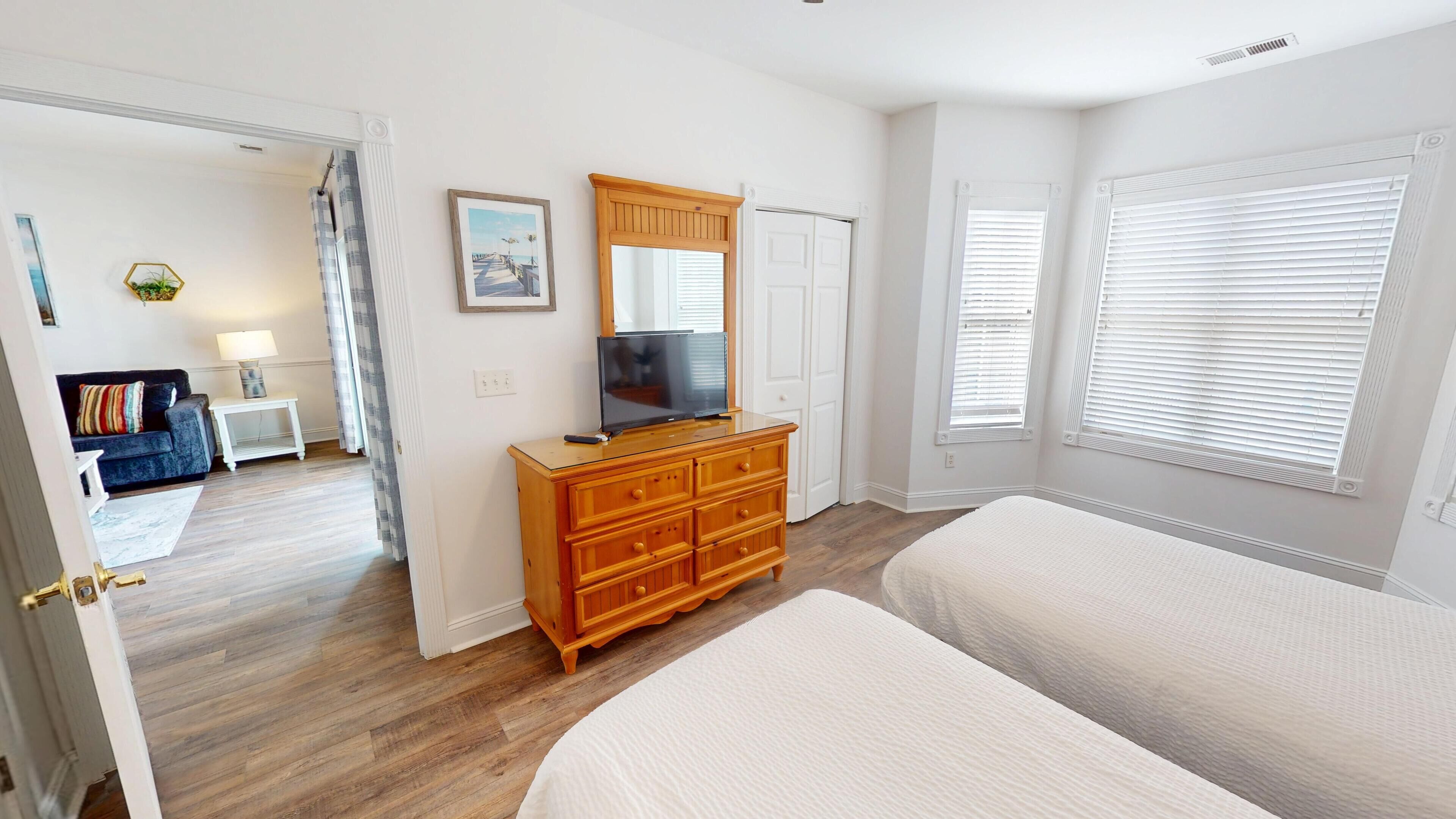 A bedroom with a wooden dresser, a television, and a large window with blinds.
