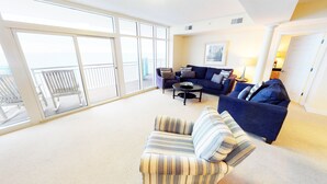 A spacious living room with a large sliding glass door leading to a balcony, a blue sofa set, a striped armchair, and a coffee table. - Ocean Blue 1101 (Myrtle Beach)