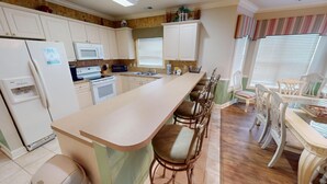 A kitchen with white cabinets, a microwave, an oven, a sink, and a bar area with stools. - Magnolia Pointe Luster Leaf 4886-101 (Myrtle Beach)