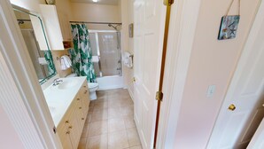 A narrow bathroom with a white sink, toilet, and shower. There is a mirror above the sink and a door on the right. - Magnolia Pointe Luster Leaf 4886-101 (Myrtle Beach)