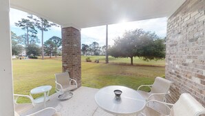 A covered patio with a brick column, white metal chairs, and a glass table. - Magnolia Pointe Luster Leaf 4886-101 (Myrtle Beach)