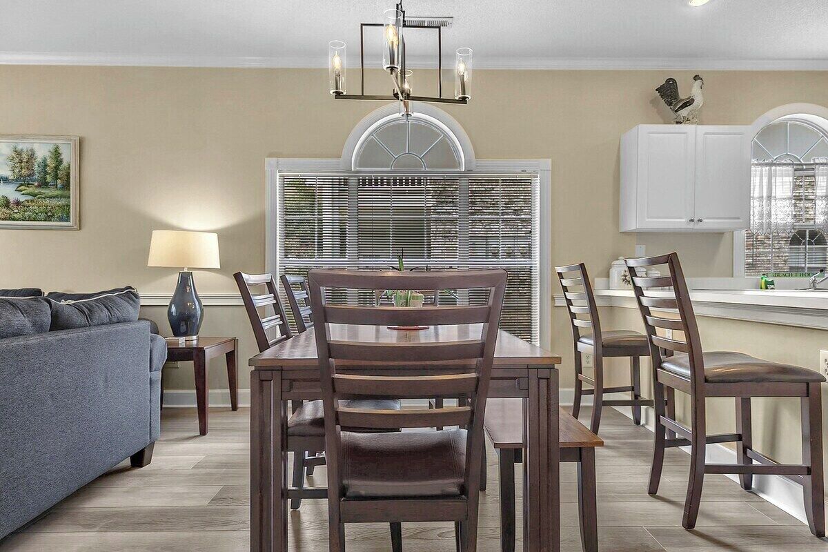 A dining area with a wooden table and chairs, a chandelier, and a window with blinds.