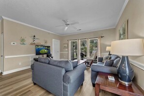 A living room with a gray sofa, a coffee table, a lamp, and a television. - Magnolia Place 4665-104 (Myrtle Beach)